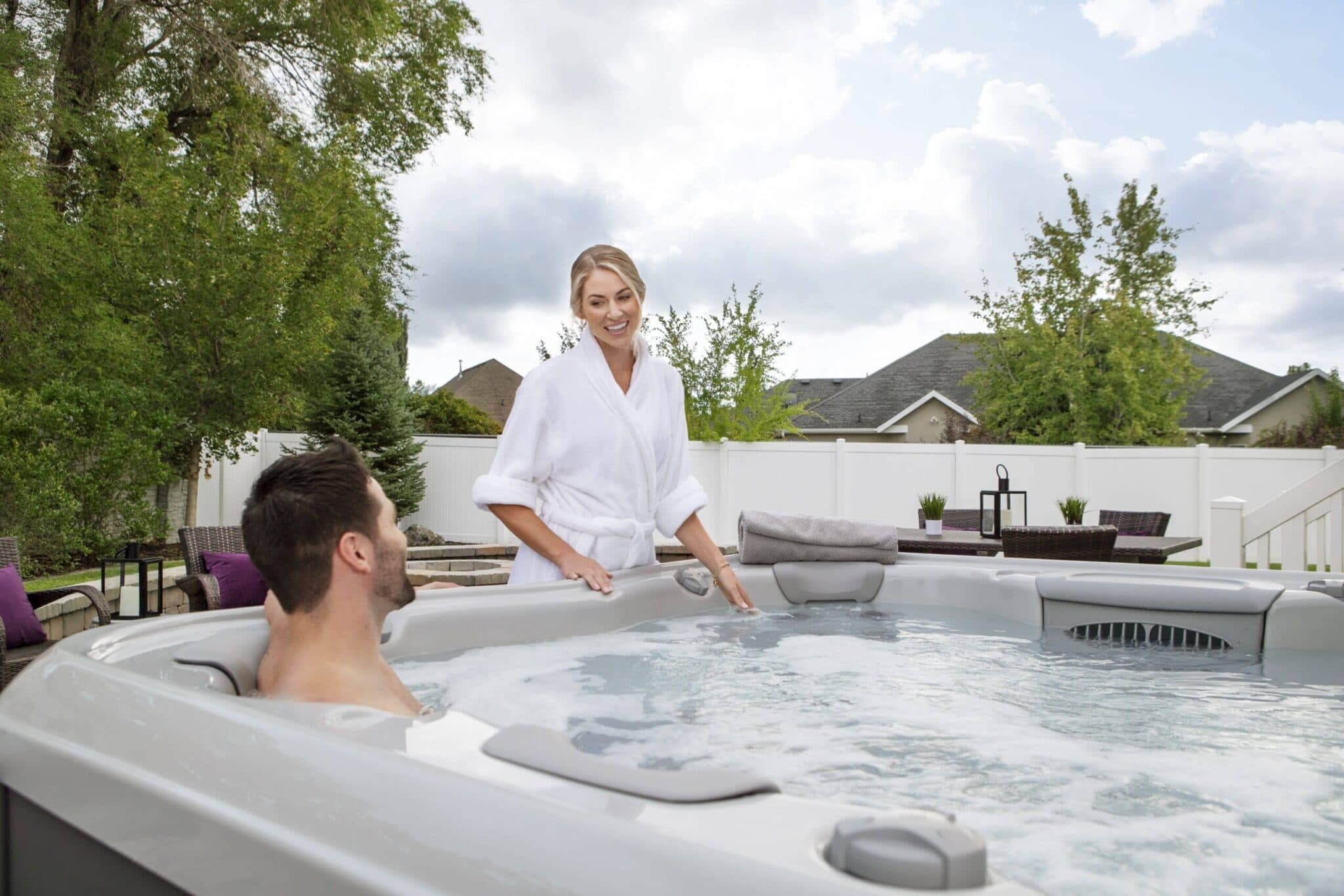A couple relaxing in a Bullfrog hot tub on a sunny backyard patio