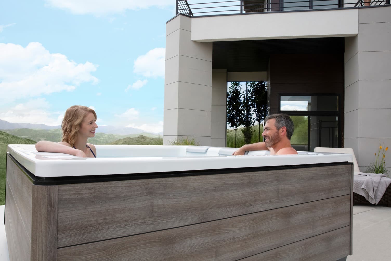 A couple relaxing in a Bullfrog hot tub beside a modern home