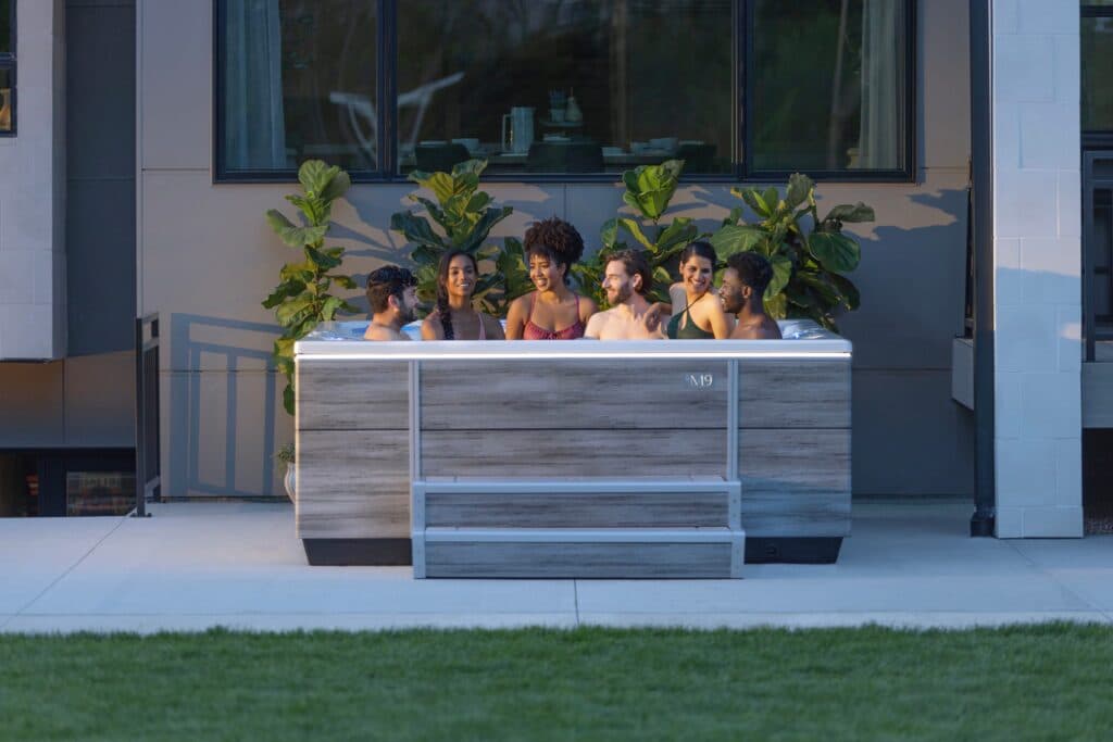 Five friends laughing together in a Bullfrog hot tub on a patio