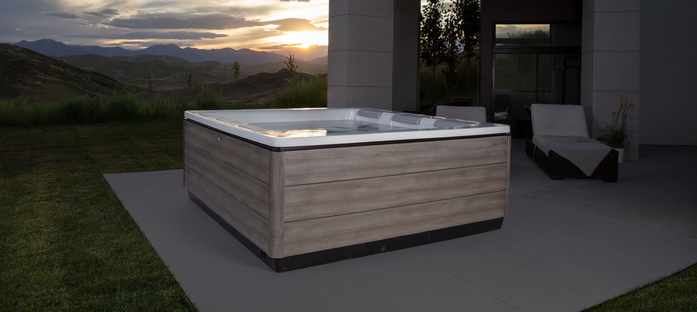 A Bullfrog STIL hot tub on a stone patio at dusk