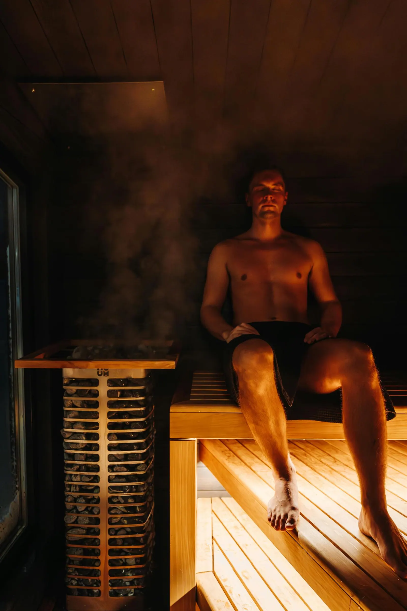 A man relaxing in a traditional sauna as steam rises from the heater stones
