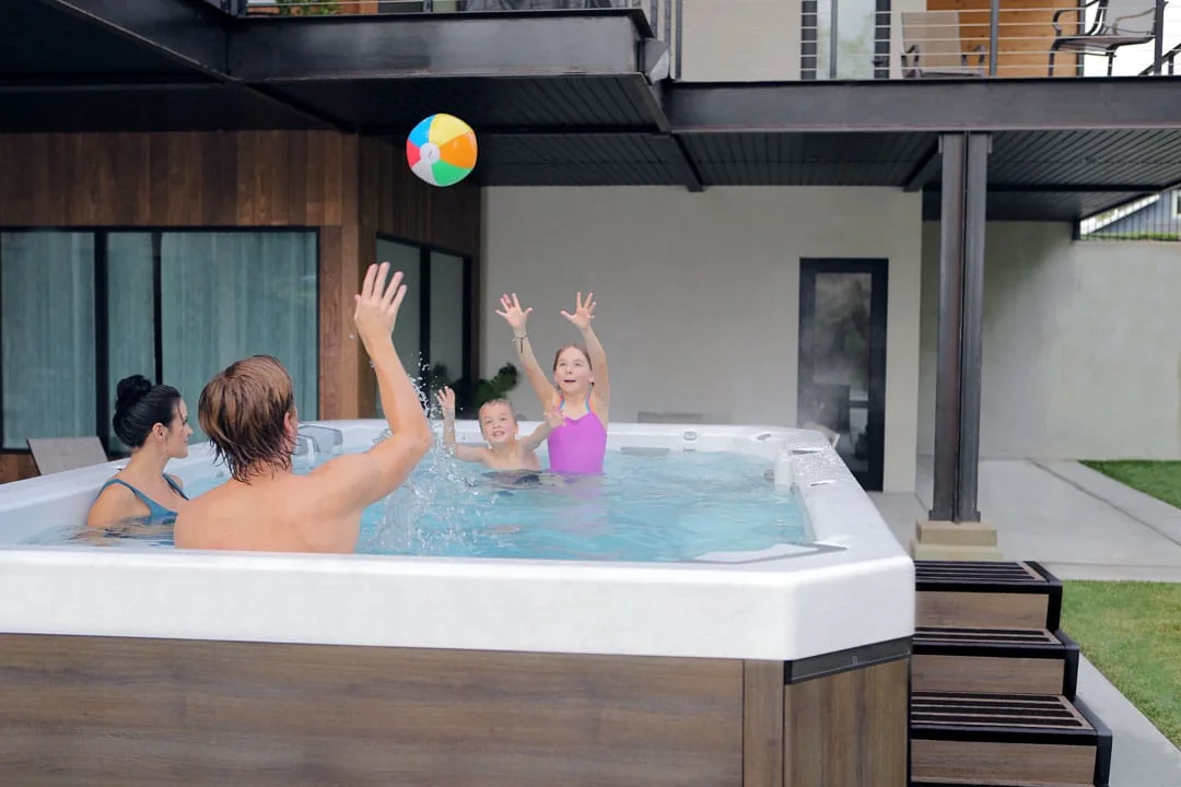 Family playing in a Bullfrog Swim Series swim spa on a covered patio